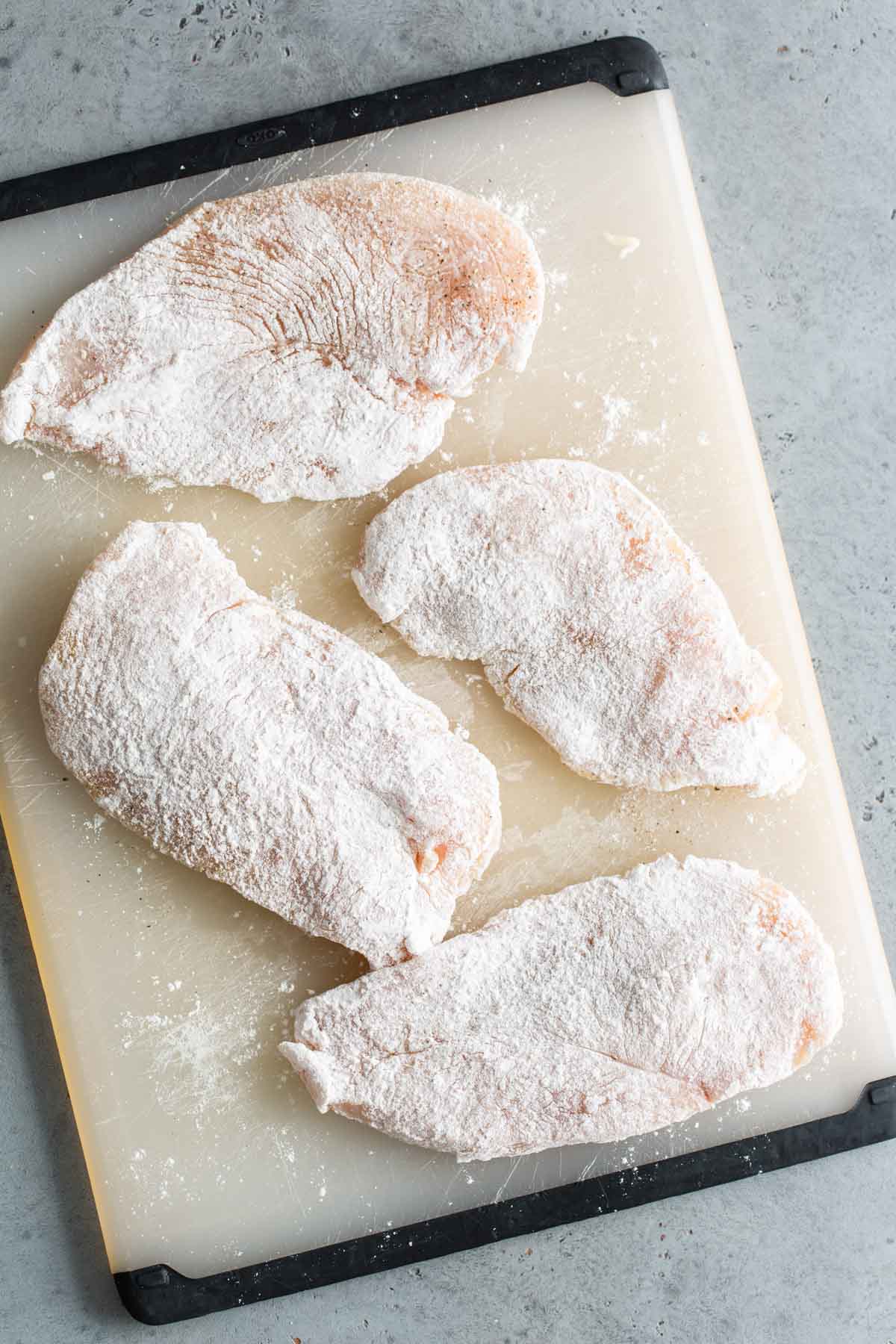 Chicken breasts on a cutting board covered in flour.