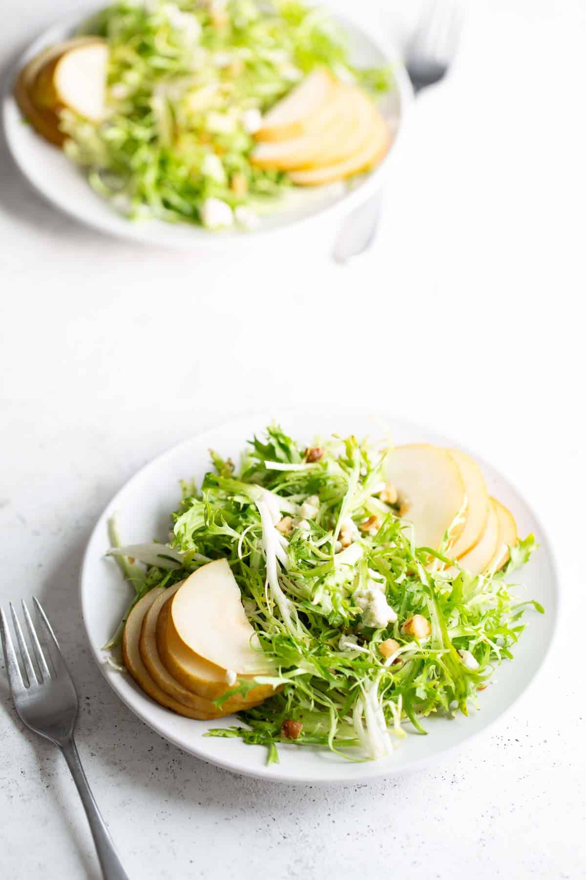 A plate of frisee salad with apples and nuts.