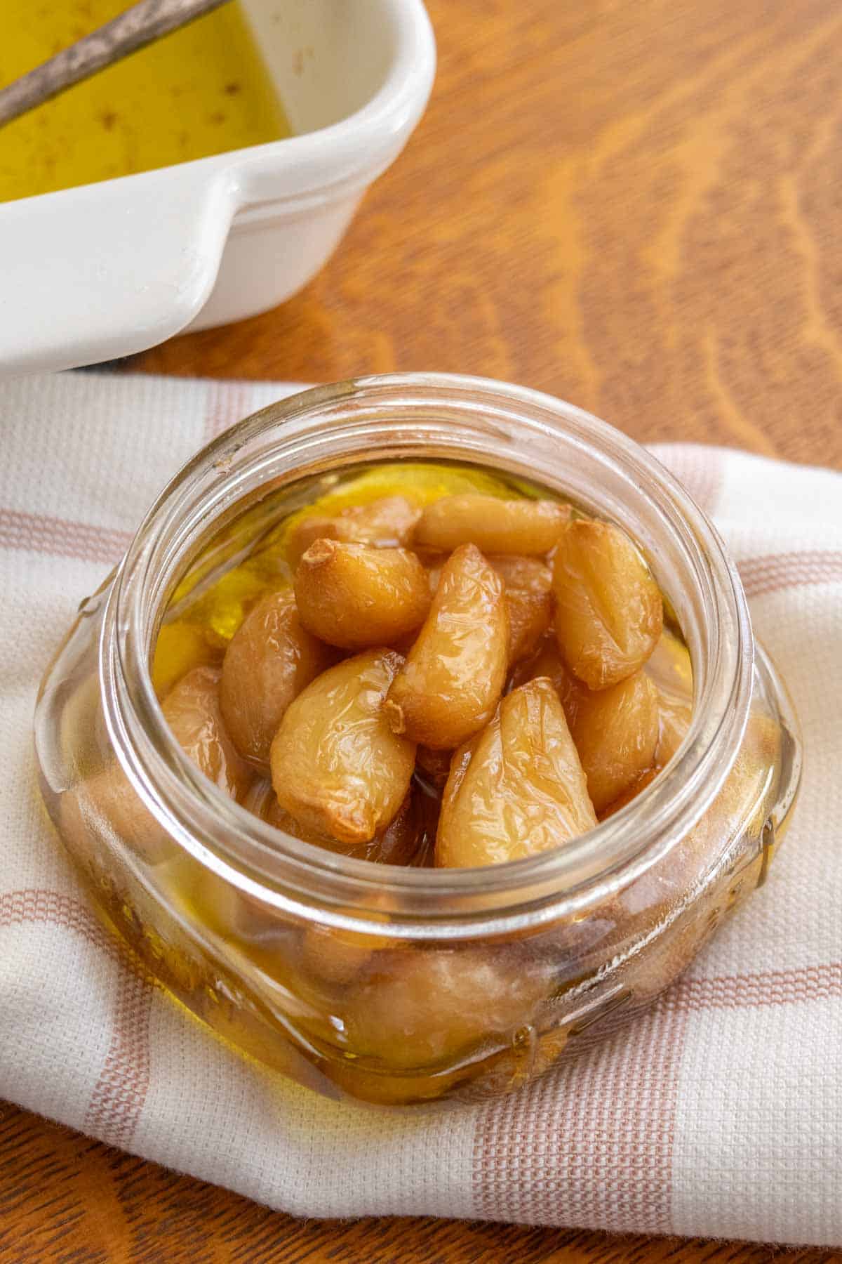 A glass jar with garlic and oil on a table.