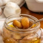 Garlic in a glass jar next to a spoon.