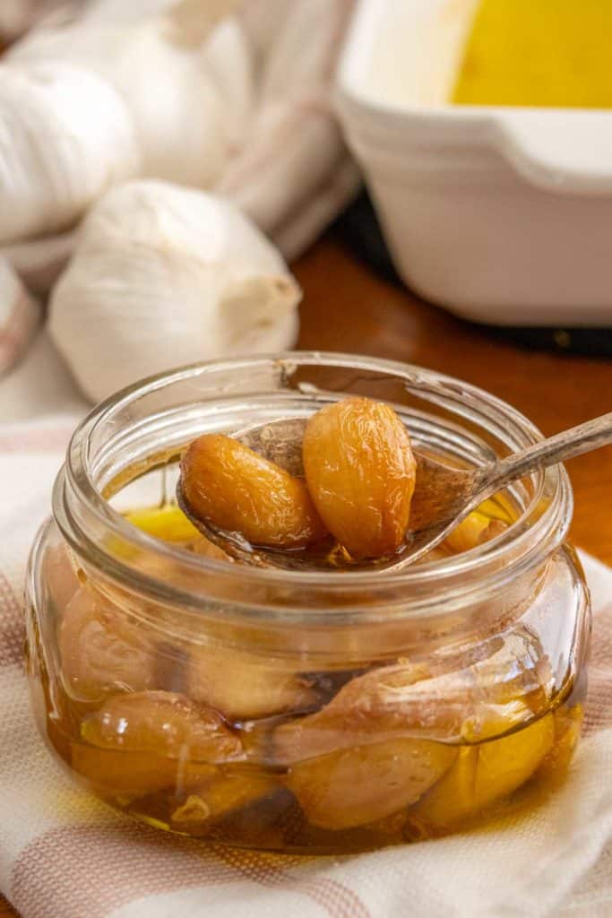 Garlic in a glass jar next to a spoon.