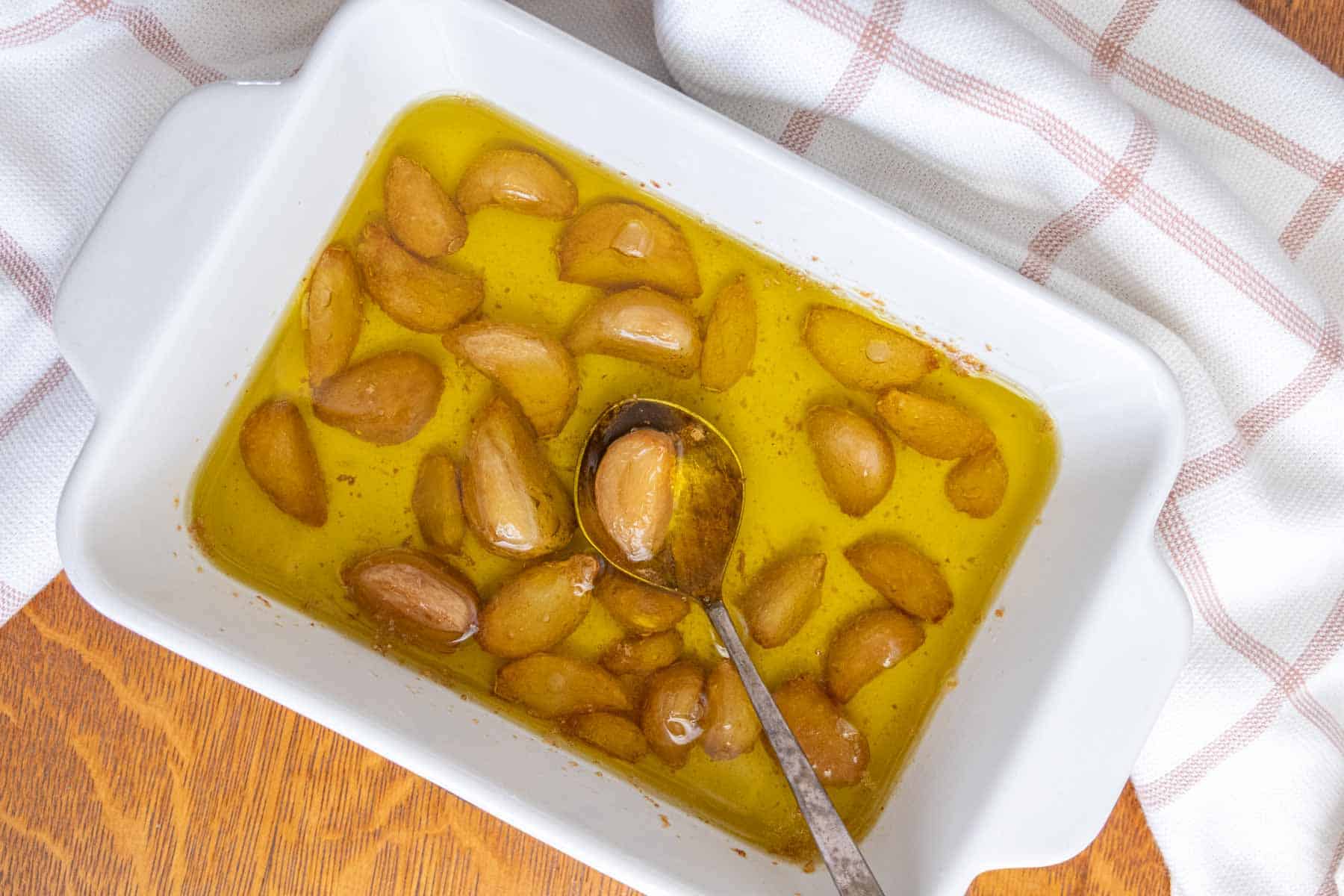 Garlic in oil in a white dish with a spoon.