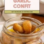 Open jar of garlic confit with several tender garlic cloves being lifted by a spoon; text above highlights a delicious garlic confit recipe on stetted.com.