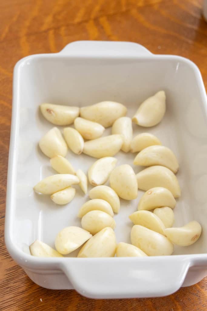 Garlic in a white baking dish on a wooden table.