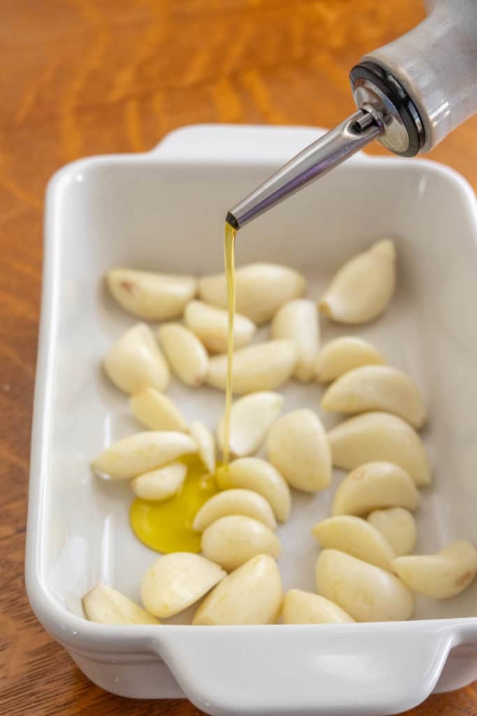 Olive oil being poured over garlic in a baking dish.