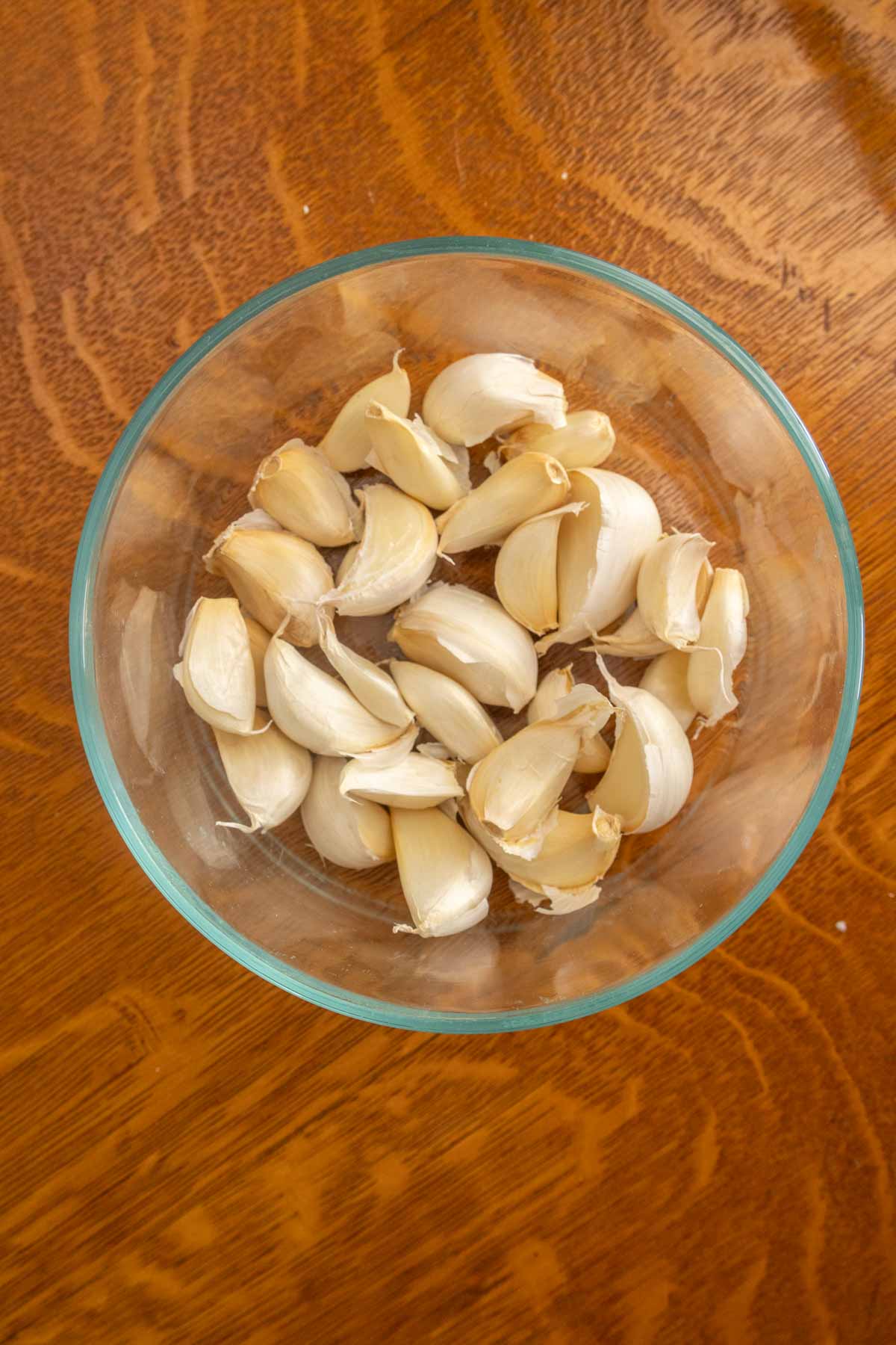 Garlic in a glass bowl on a wooden table.