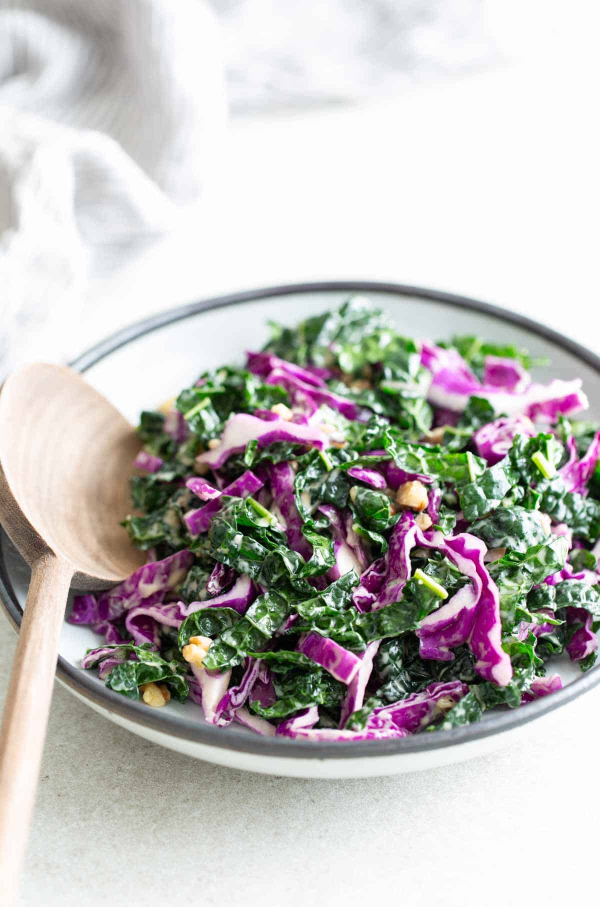 Kale salad in a bowl with a wooden spoon.