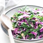 A bowl of kale salad with a wooden spoon.