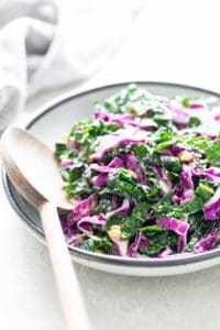 A bowl of kale salad with a wooden spoon.