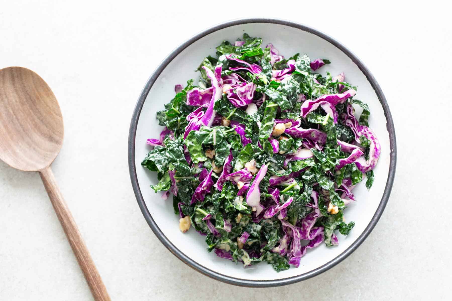 Kale slaw in a bowl with a wooden spoon.
