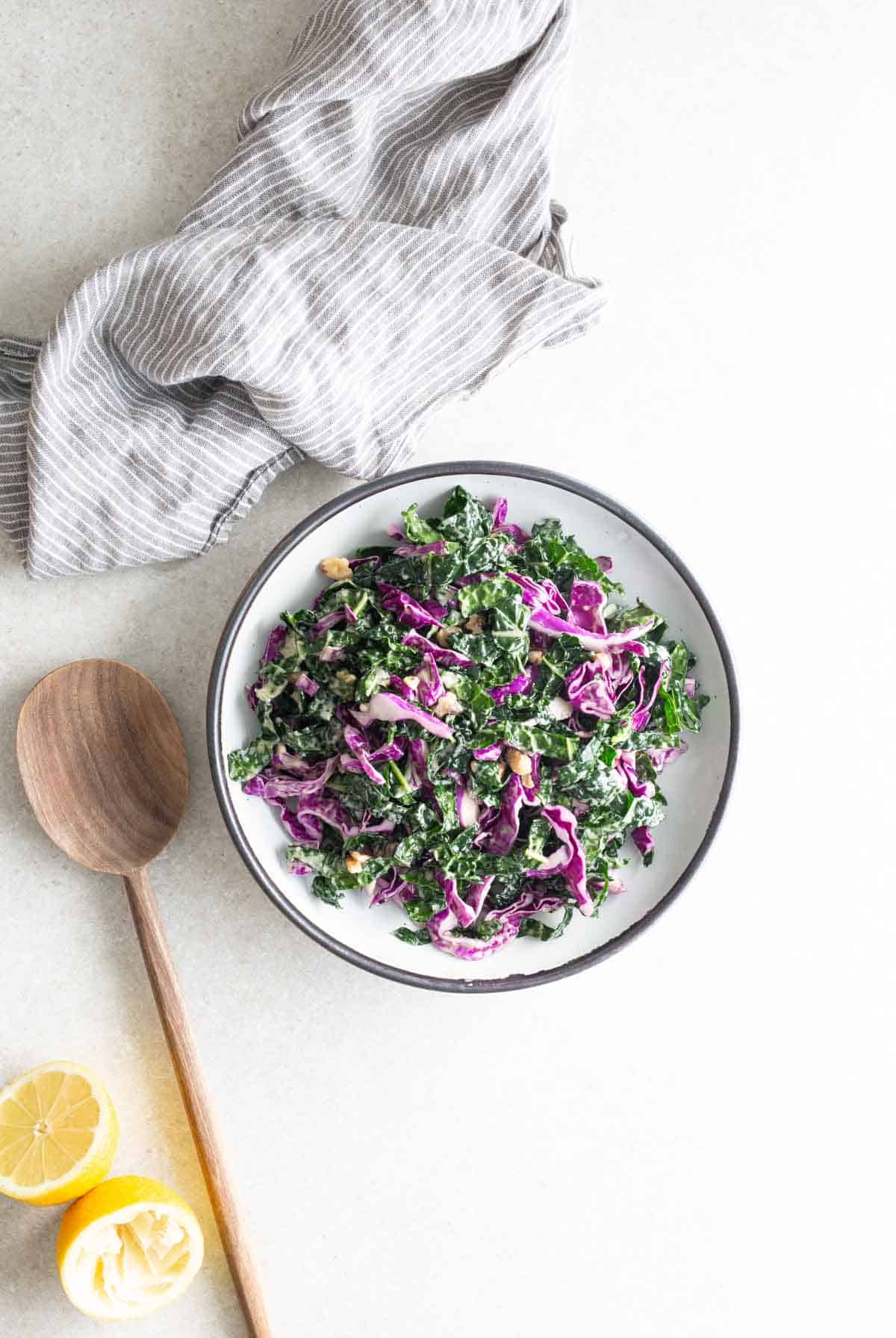 A bowl of kale salad with lemon slices and a wooden spoon.