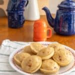 A plate of mini pancakes on a table next to a teapot.