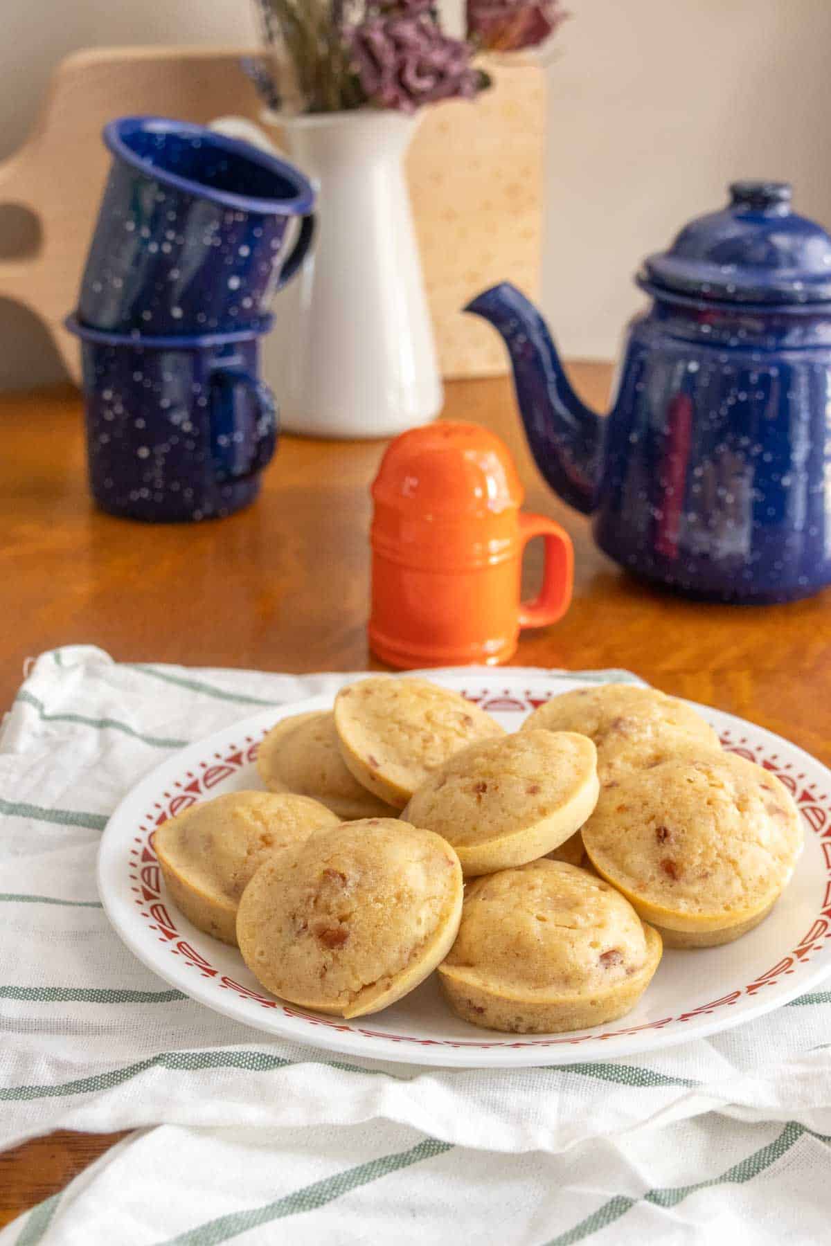A plate of mini pancakes on a table next to a teapot.