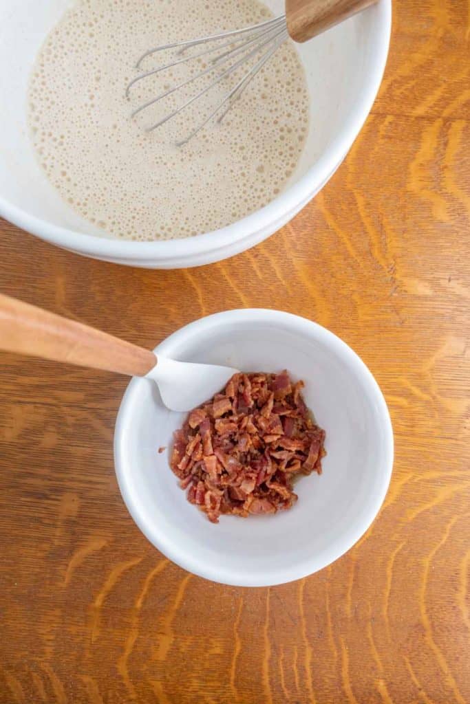 Bacon in a bowl next to a whisk.