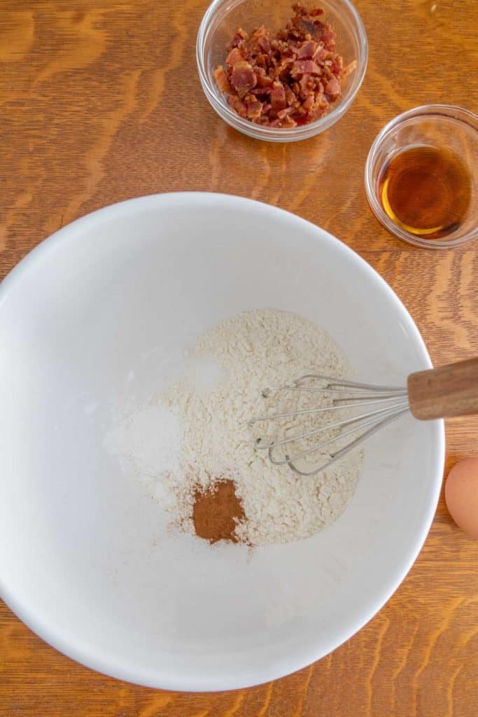A white bowl with flour, eggs, sugar, and a whisk.