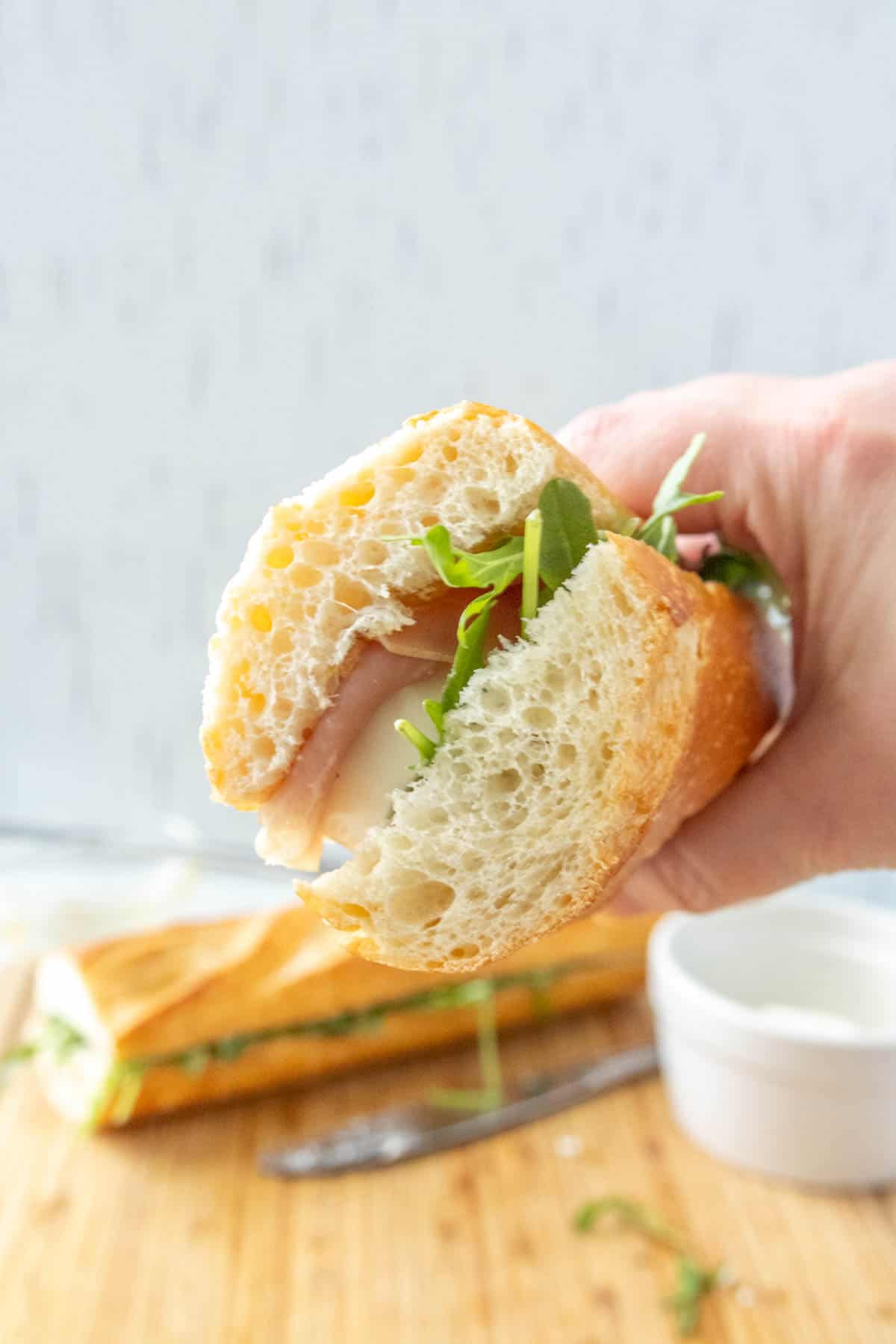 A person holding a sandwich on a cutting board.