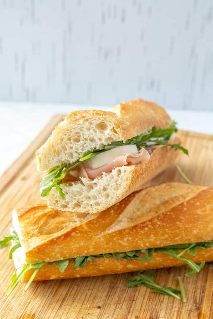 A sandwich with prosciutto and arugula on a wooden cutting board.