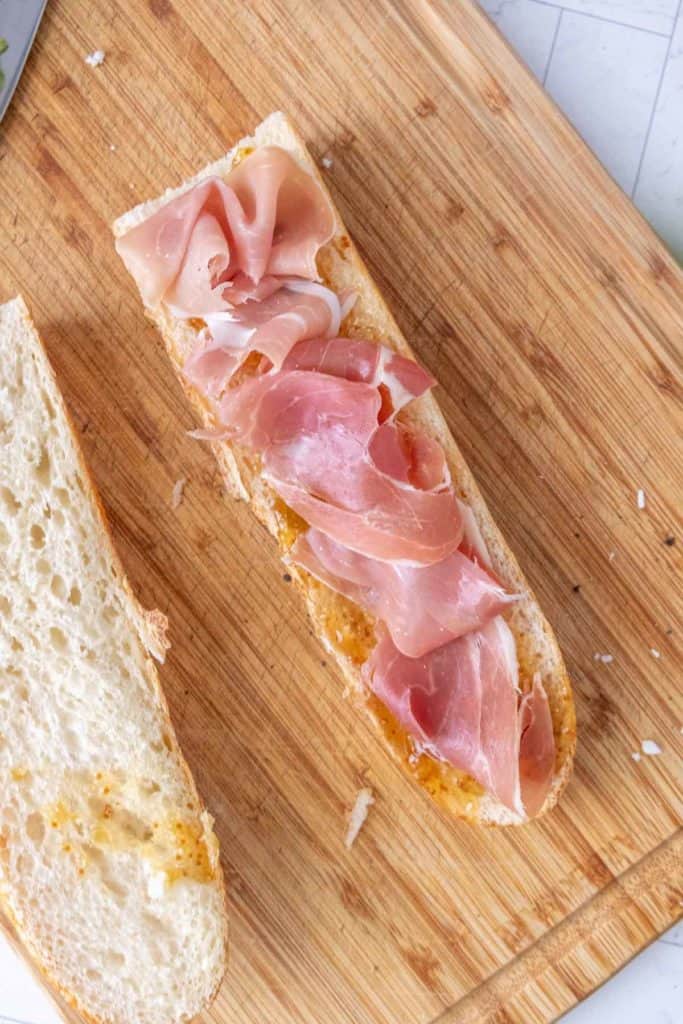 Two slices of bread with prosciutto and olives on a cutting board.