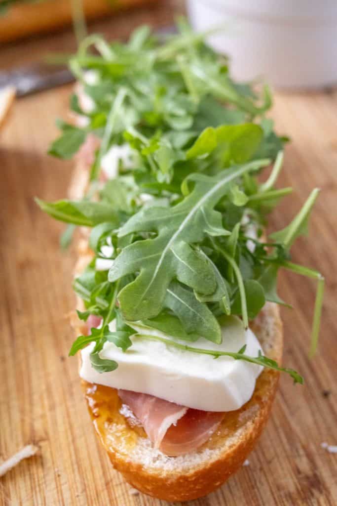 A sandwich with prosciutto and arugula on a wooden board.