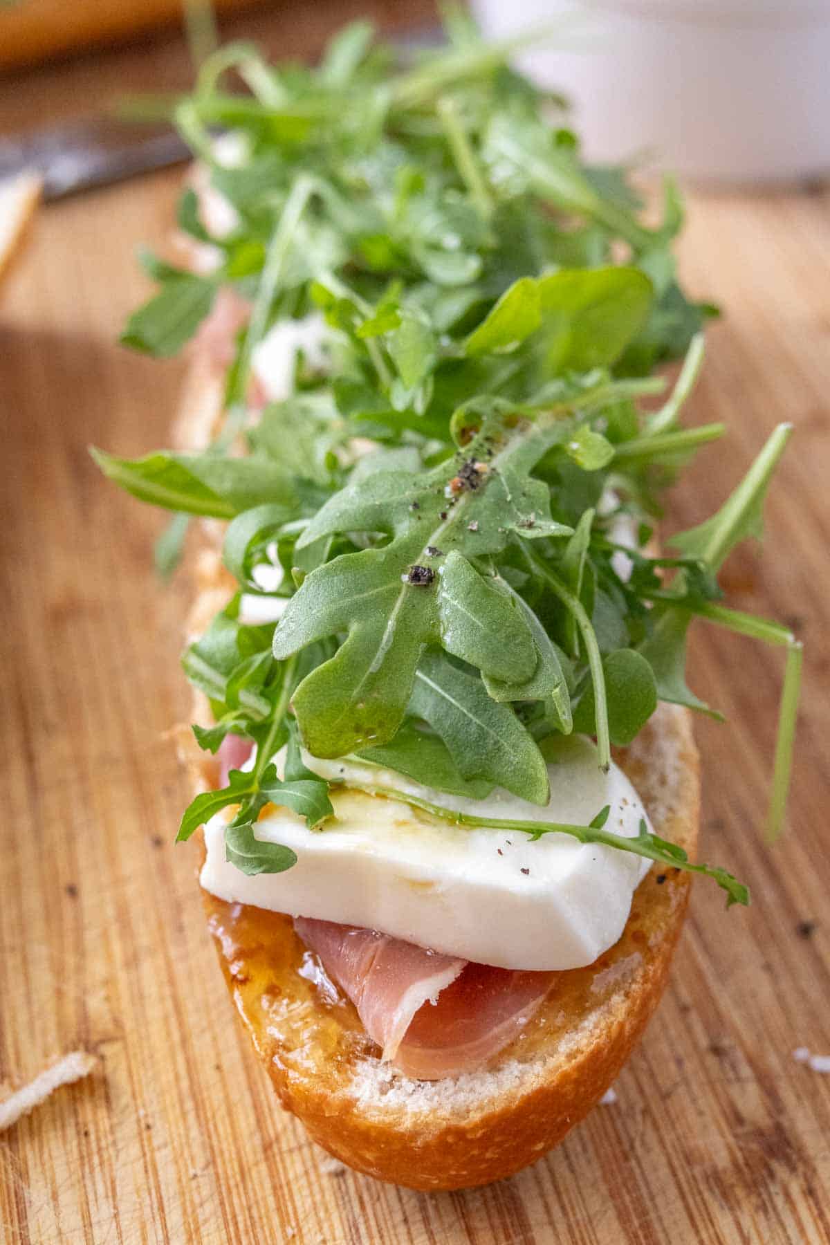 A sandwich with ham, cheese and arugula on a wooden cutting board.