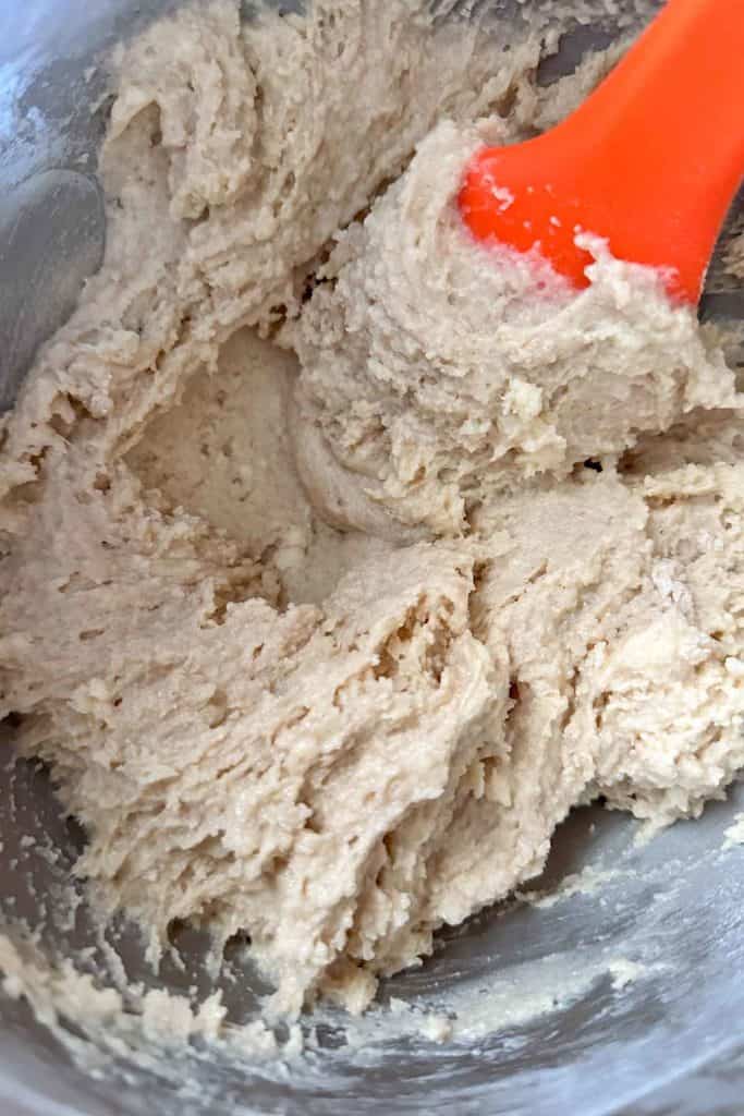 A bowl of dough with an orange spatula.