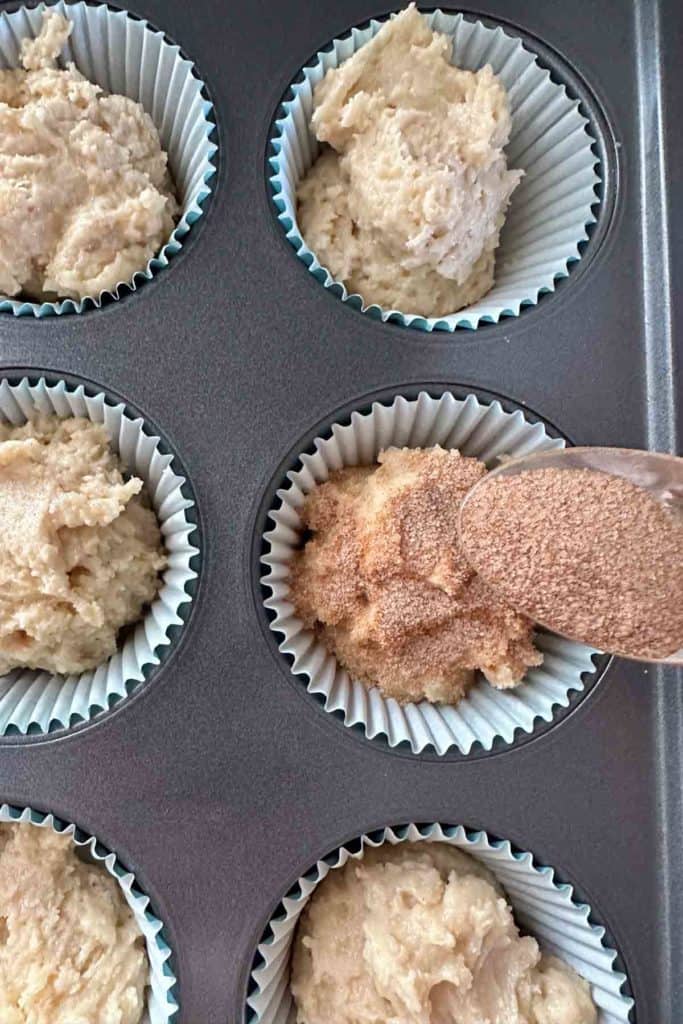 Muffins in a muffin tin with a scoop of sugar.