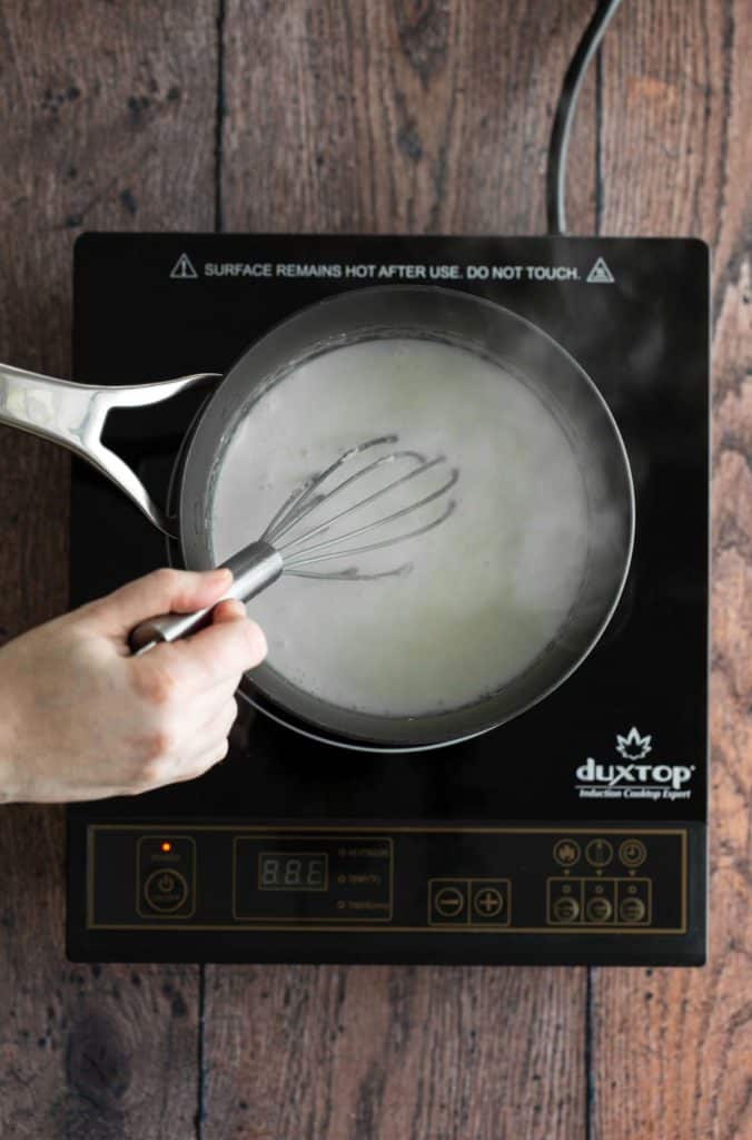 A person whisking milk in a pan on an induction stove.