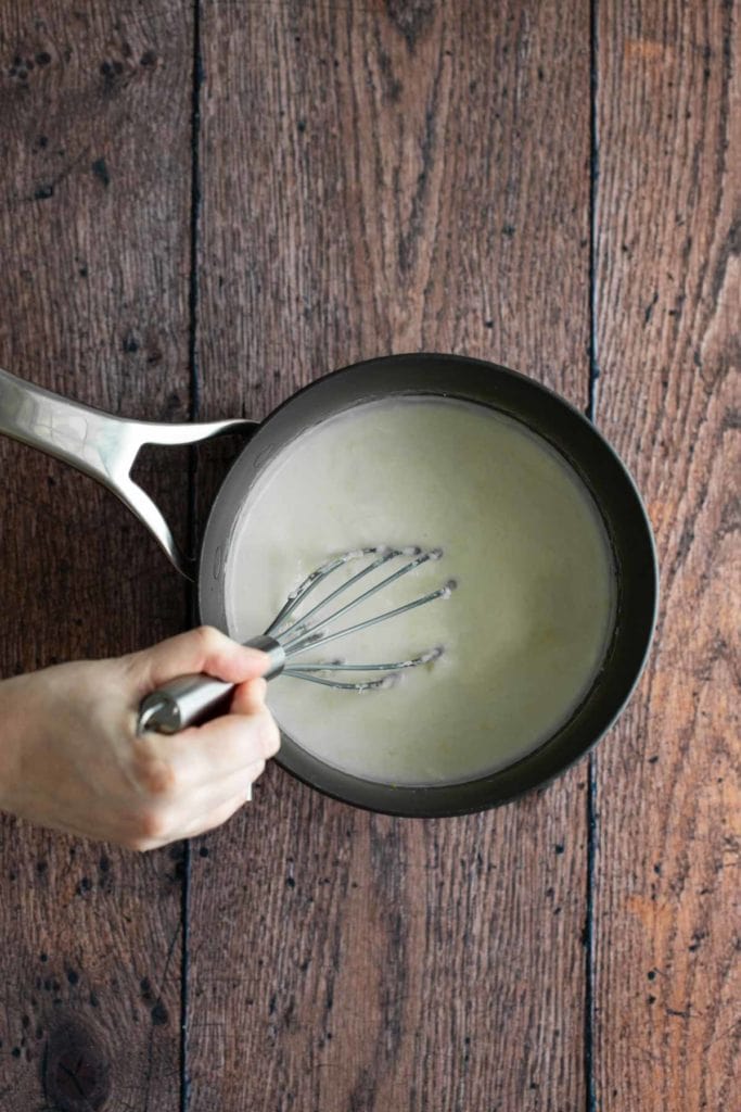 A person whisking a mixture in a pan on a wooden surface.