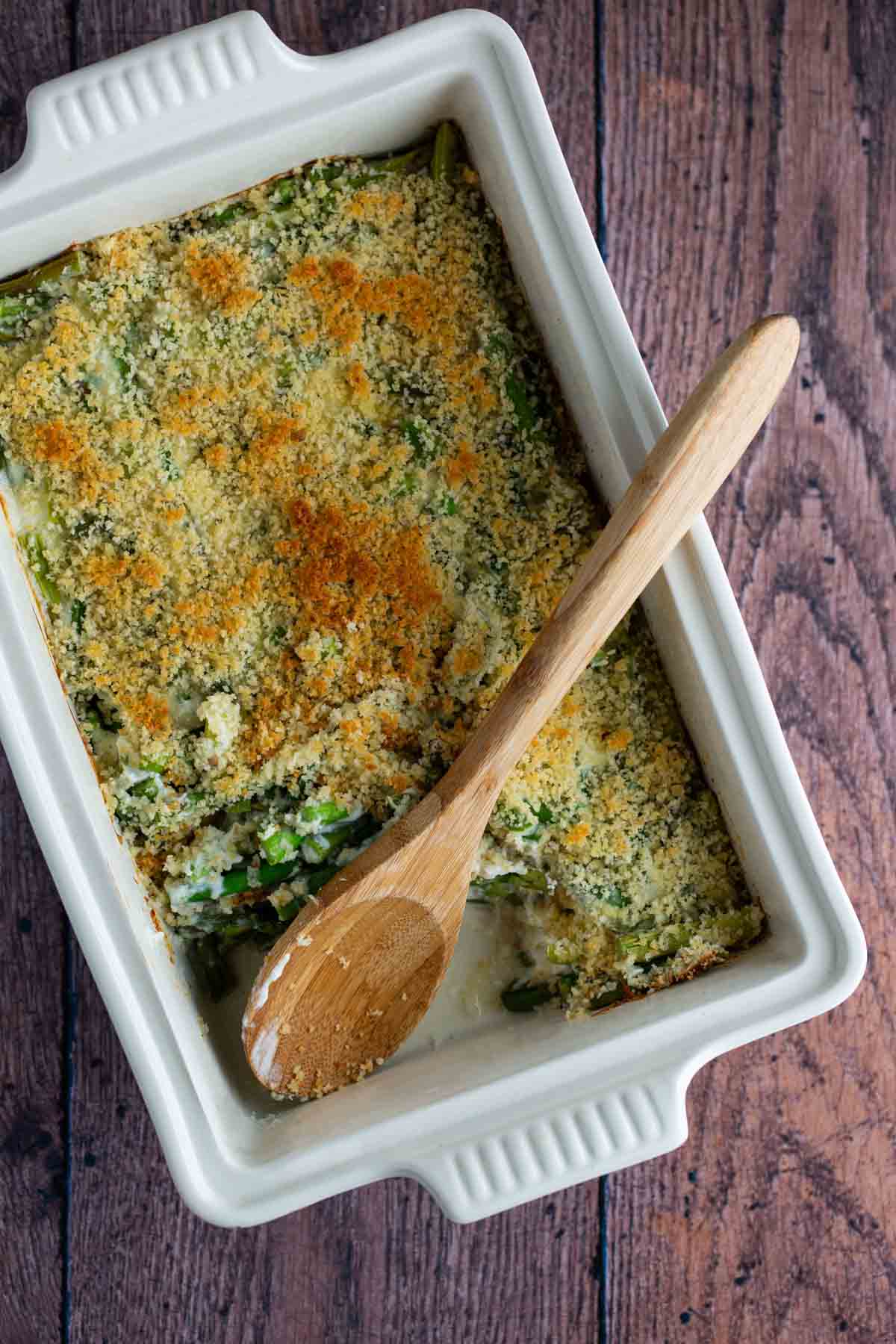 Baked casserole in a white dish with a wooden spoon.