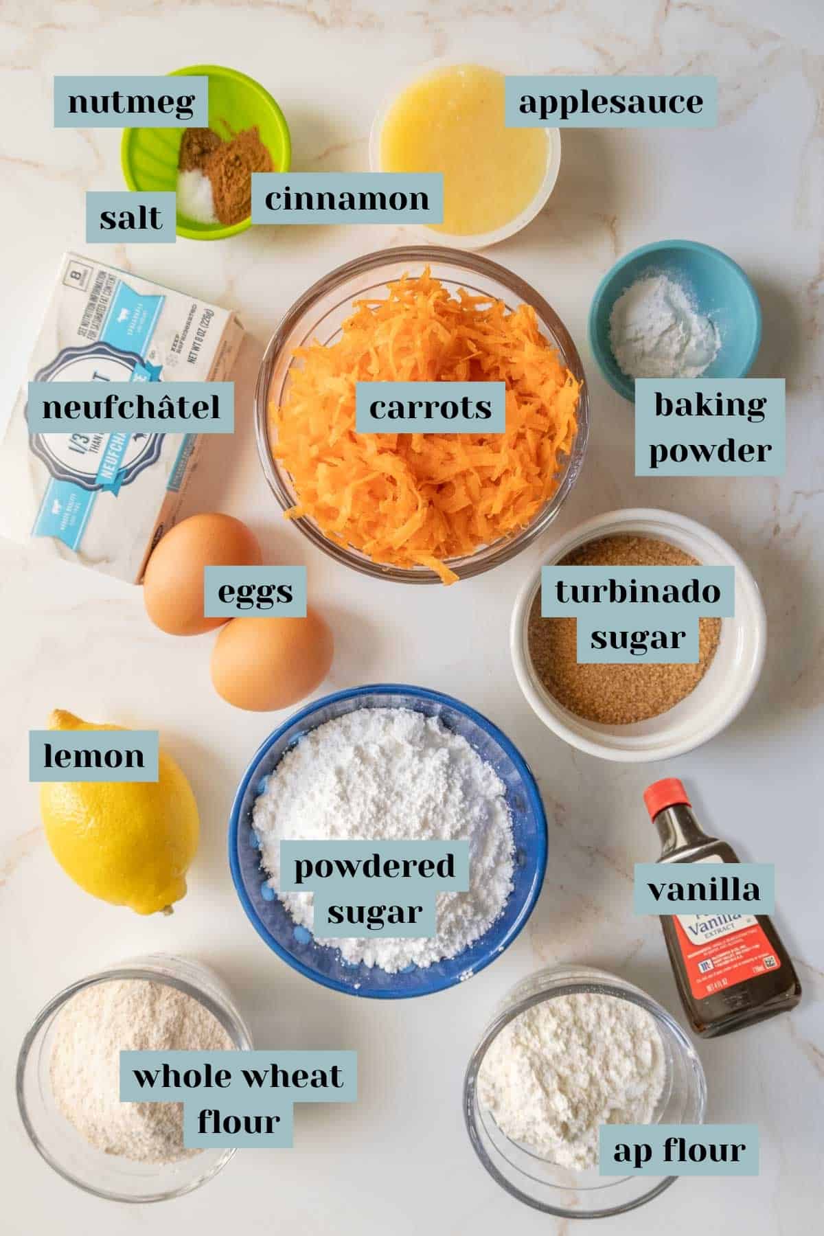 Ingredients for baking arranged on a counter with labels indicating each item, such as carrots, flour, eggs, and spices.