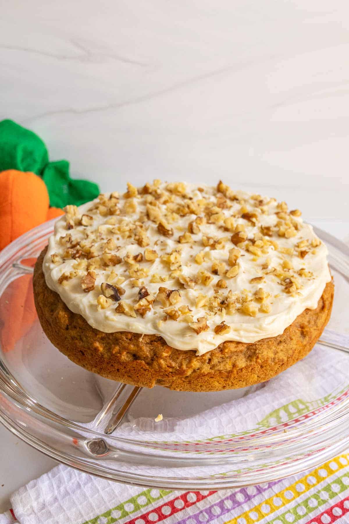 A carrot cake on a glass cake stand.