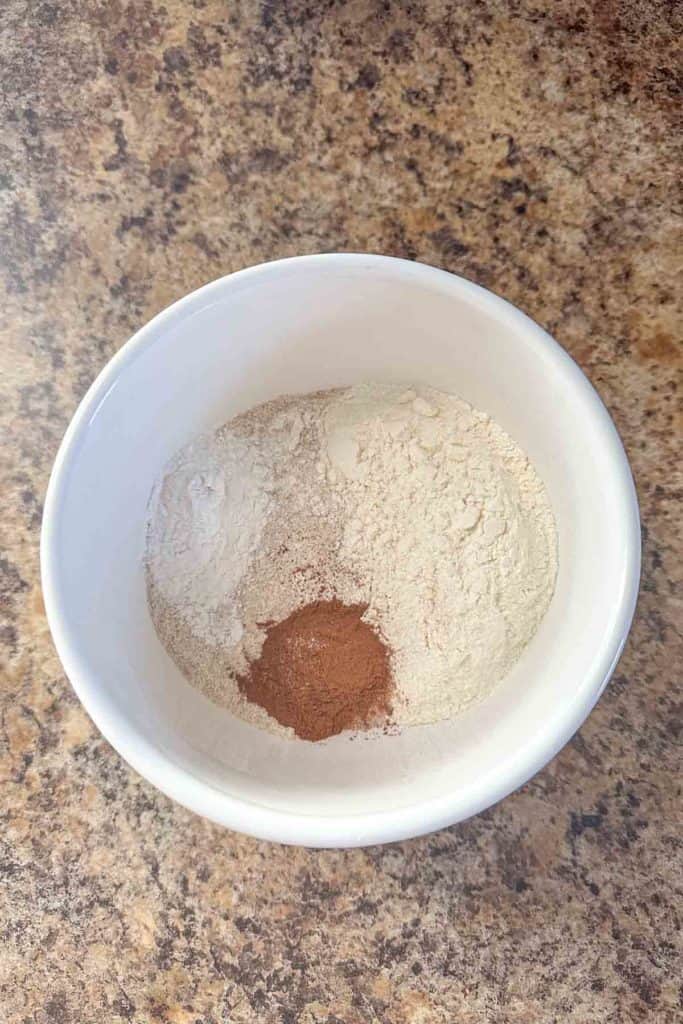 A bowl containing flour and a scoop of cocoa powder on a kitchen countertop.