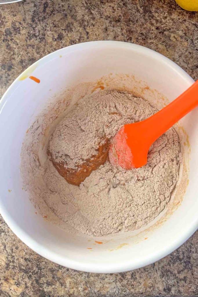 Mixing wet and dry ingredients in a bowl with a red spatula.