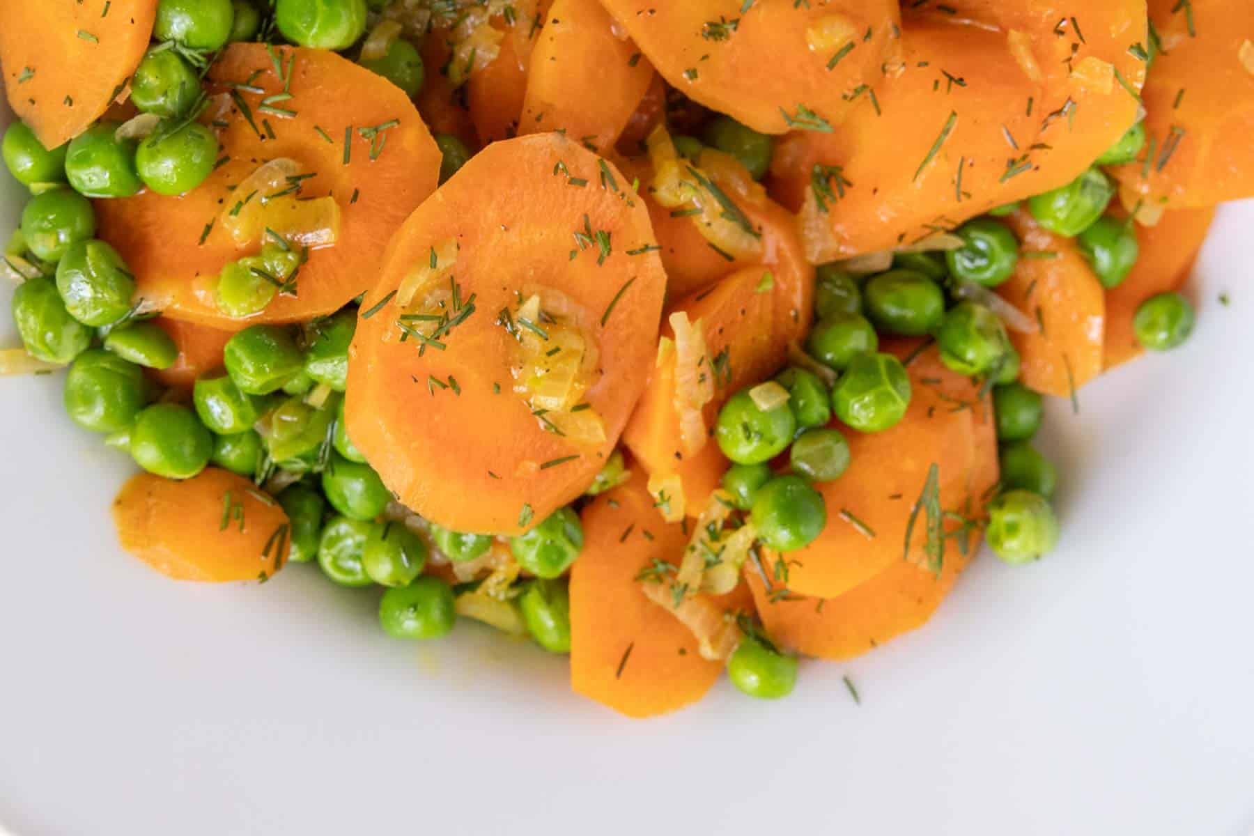 Sliced carrots and green peas seasoned with herbs on a white plate.
