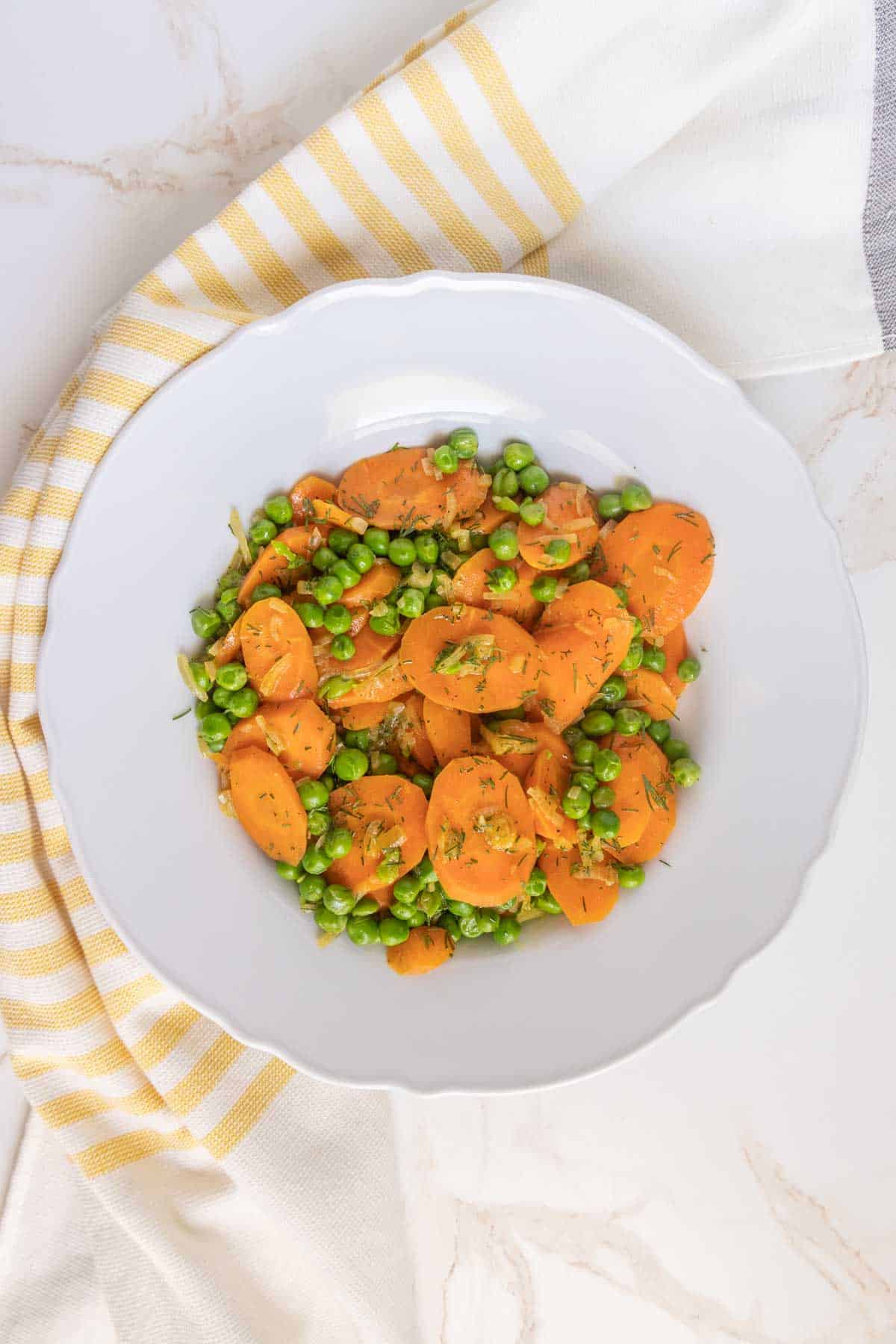 A plate of sliced carrots and green peas on a table with a striped napkin.