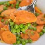 A spoonful of cooked peas and sliced carrots garnished with herbs.