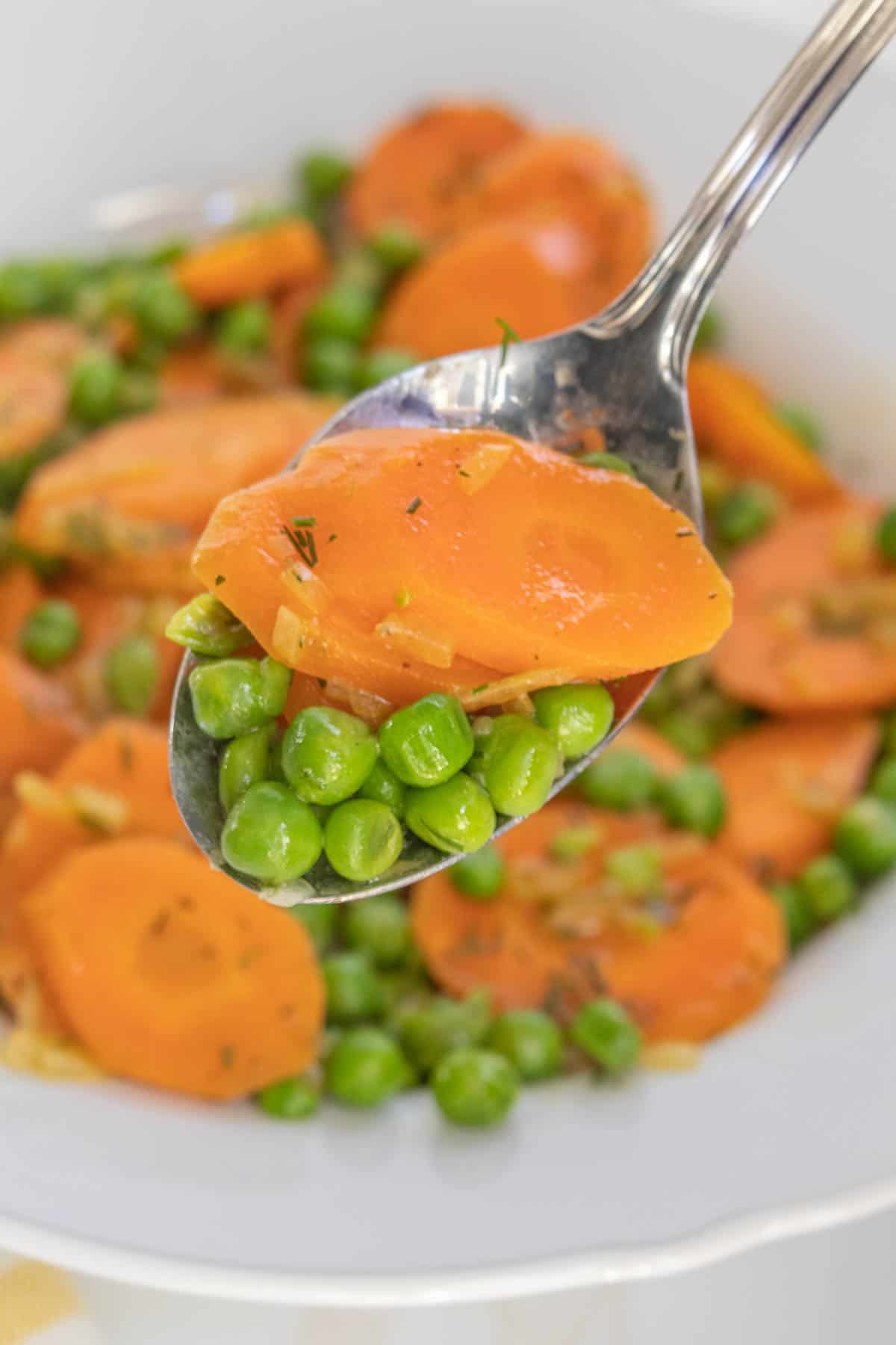 A spoonful of cooked peas and sliced carrots garnished with herbs.