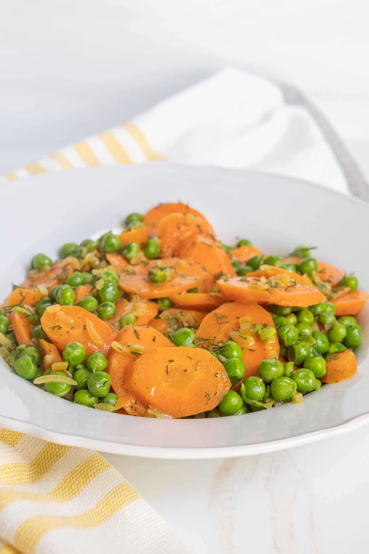 A plate of sliced carrots and green peas garnished with herbs.