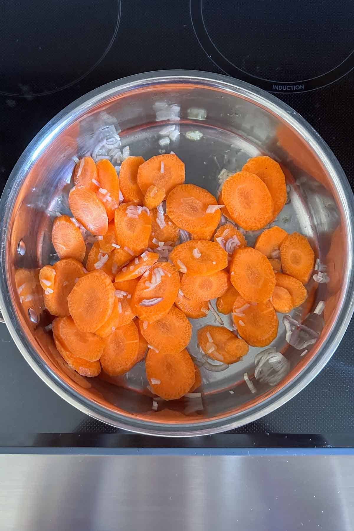 Sliced carrots in a stainless steel bowl on an induction stove top.