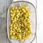 Diced potatoes drying on a mesh strainer over a white countertop.