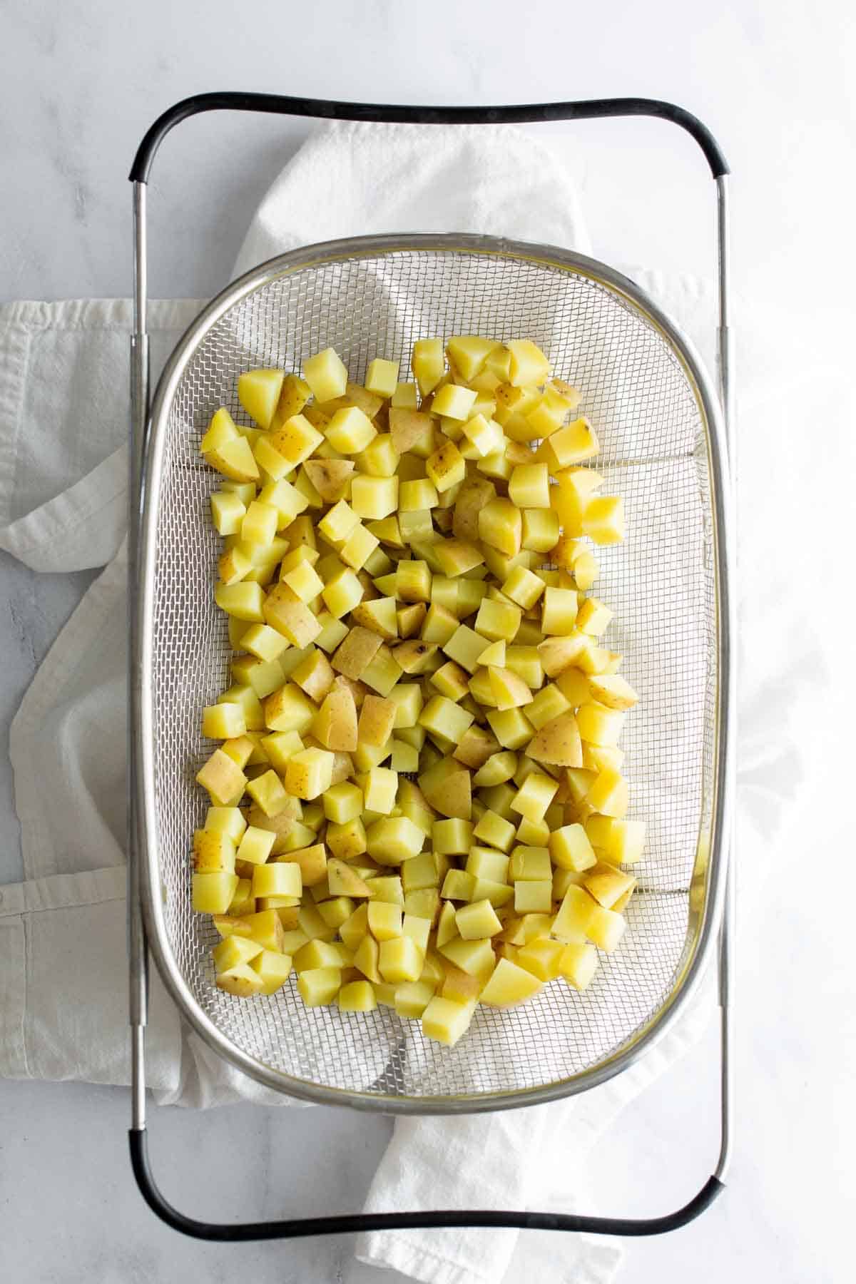 Diced potatoes drying on a mesh strainer over a white countertop.