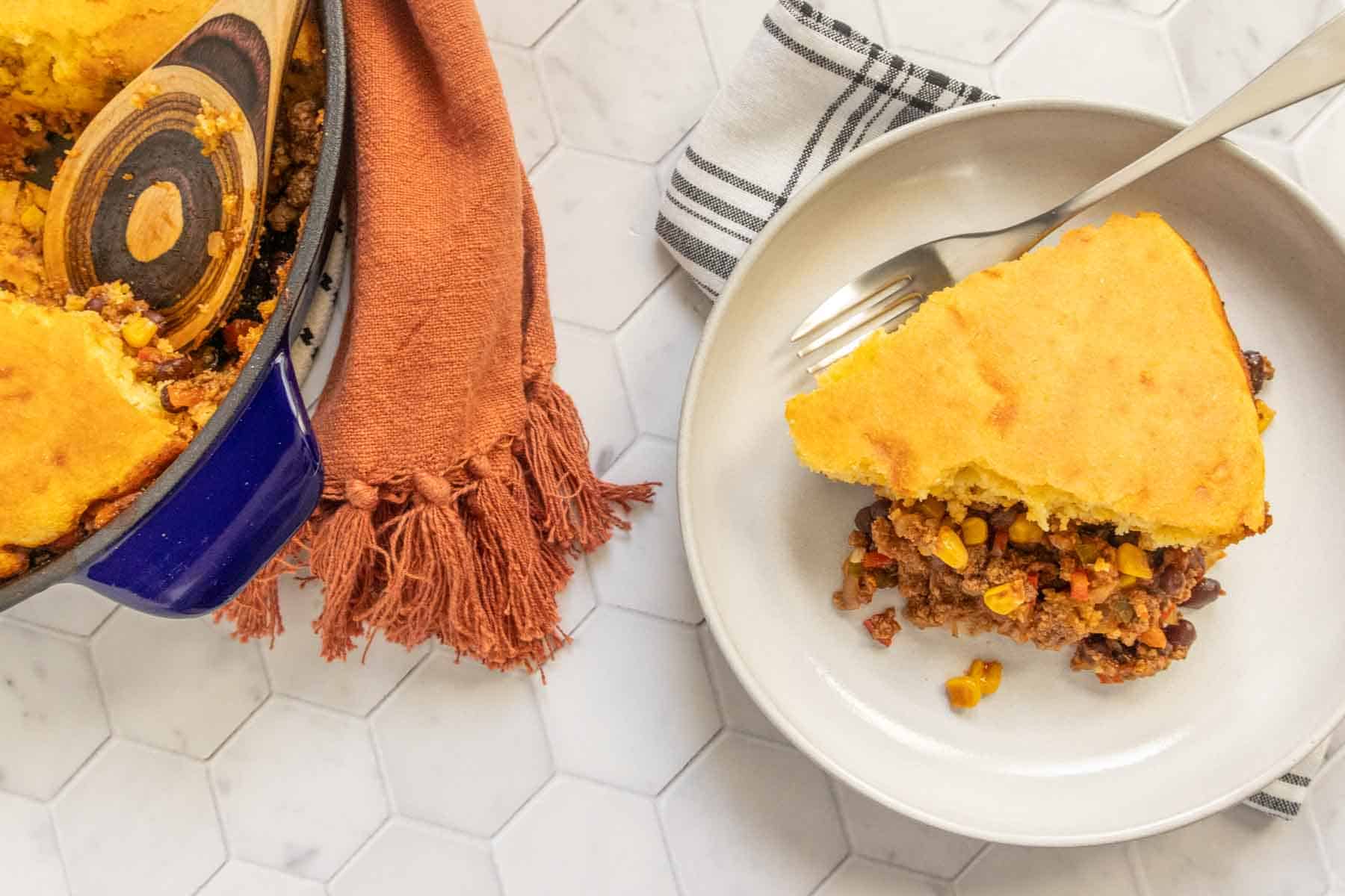 A serving of cornbread-topped casserole on a plate, with the baking dish alongside.