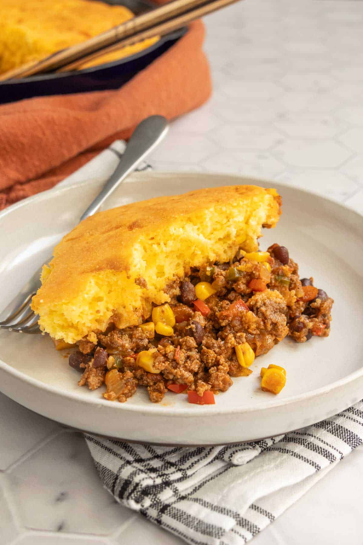 A slice of cornbread casserole with a beef and vegetable filling on a white plate.