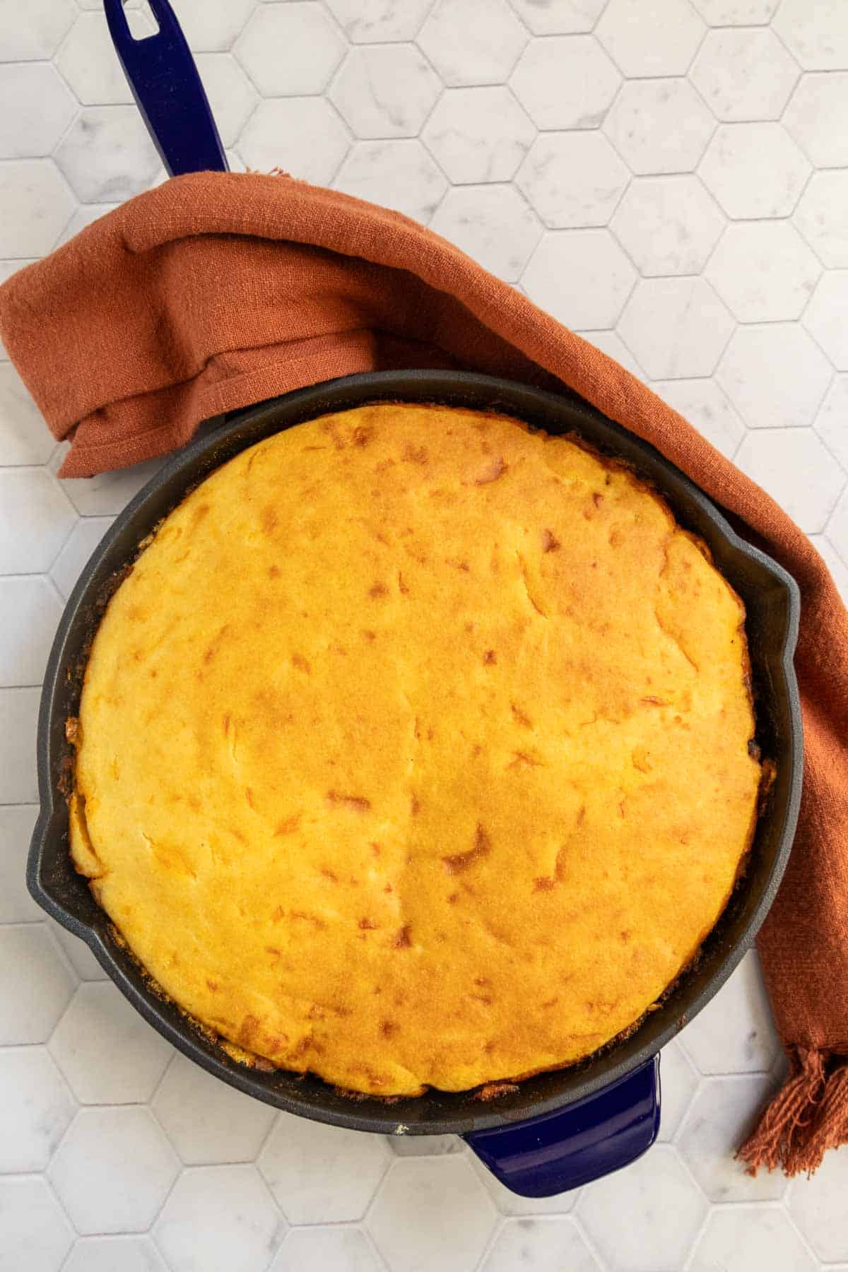 A freshly baked cornbread in a cast-iron skillet with a kitchen towel on the side.