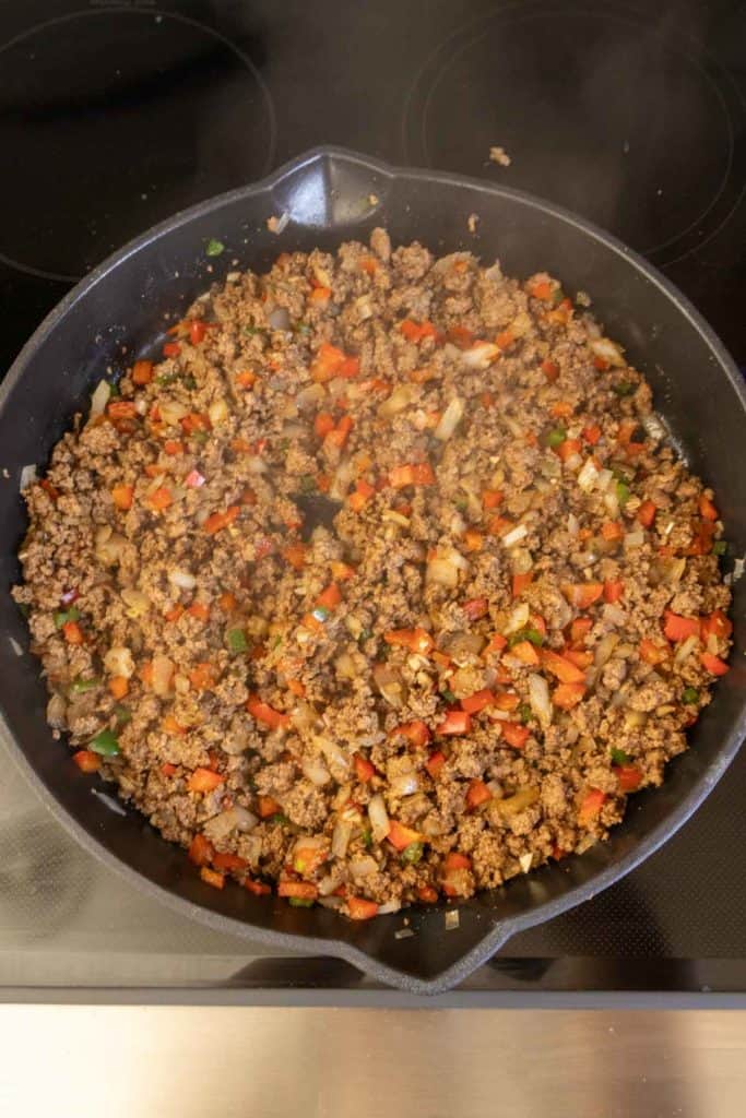 Ground meat with diced vegetables cooking in a skillet.