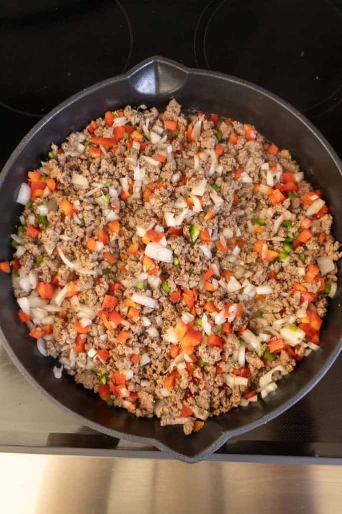 Cooked ground meat with diced onions and bell peppers in a cast-iron skillet.