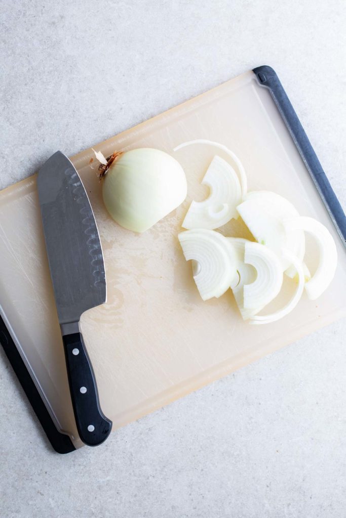 A knife and sliced onions on a cutting board.