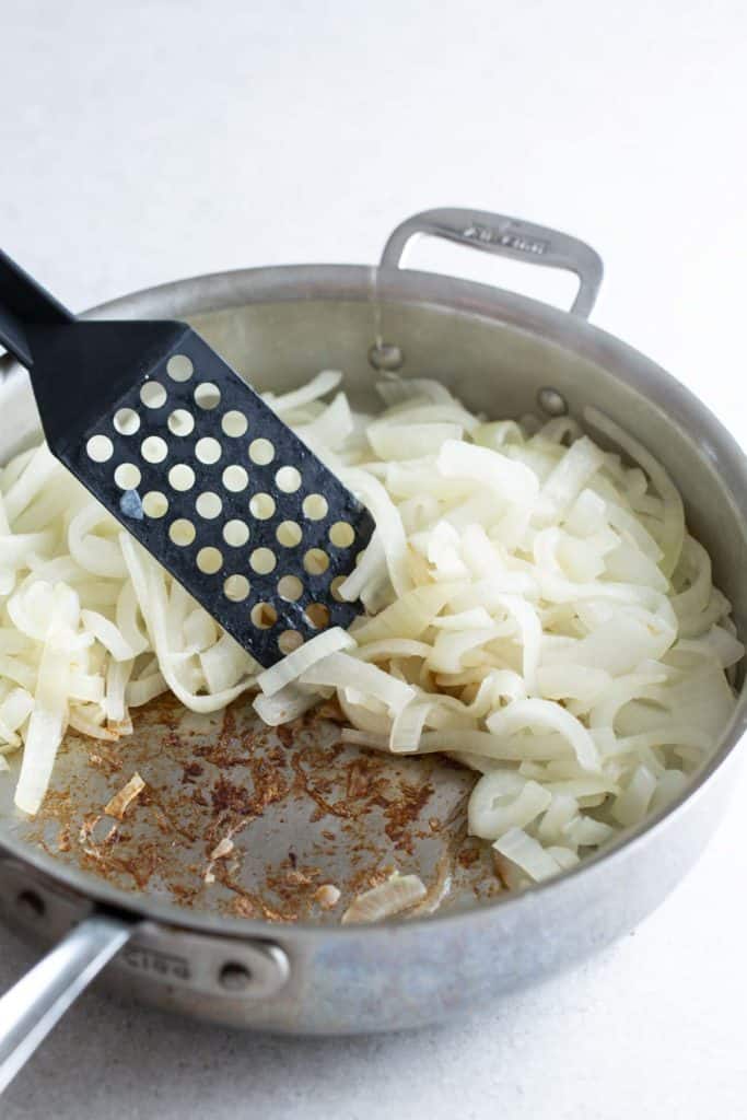 Sautéed onions in a stainless steel pan with a slotted spatula.