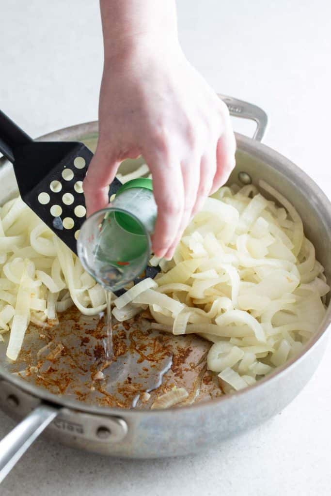 Pouring liquid into a pan of sautéed onions.