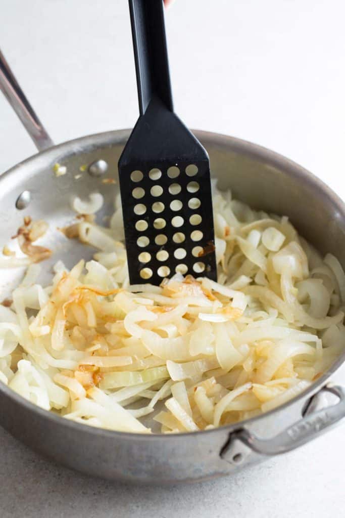 Sautéed onions in a pan with a slotted spatula.